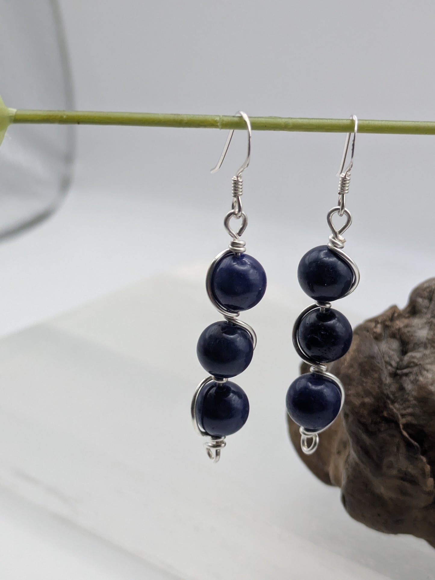 Close-up of silver wrapped Lapis Lazuli earrings with three deep blue gemstone beads in a vertical drop design, displayed on a neutral background.