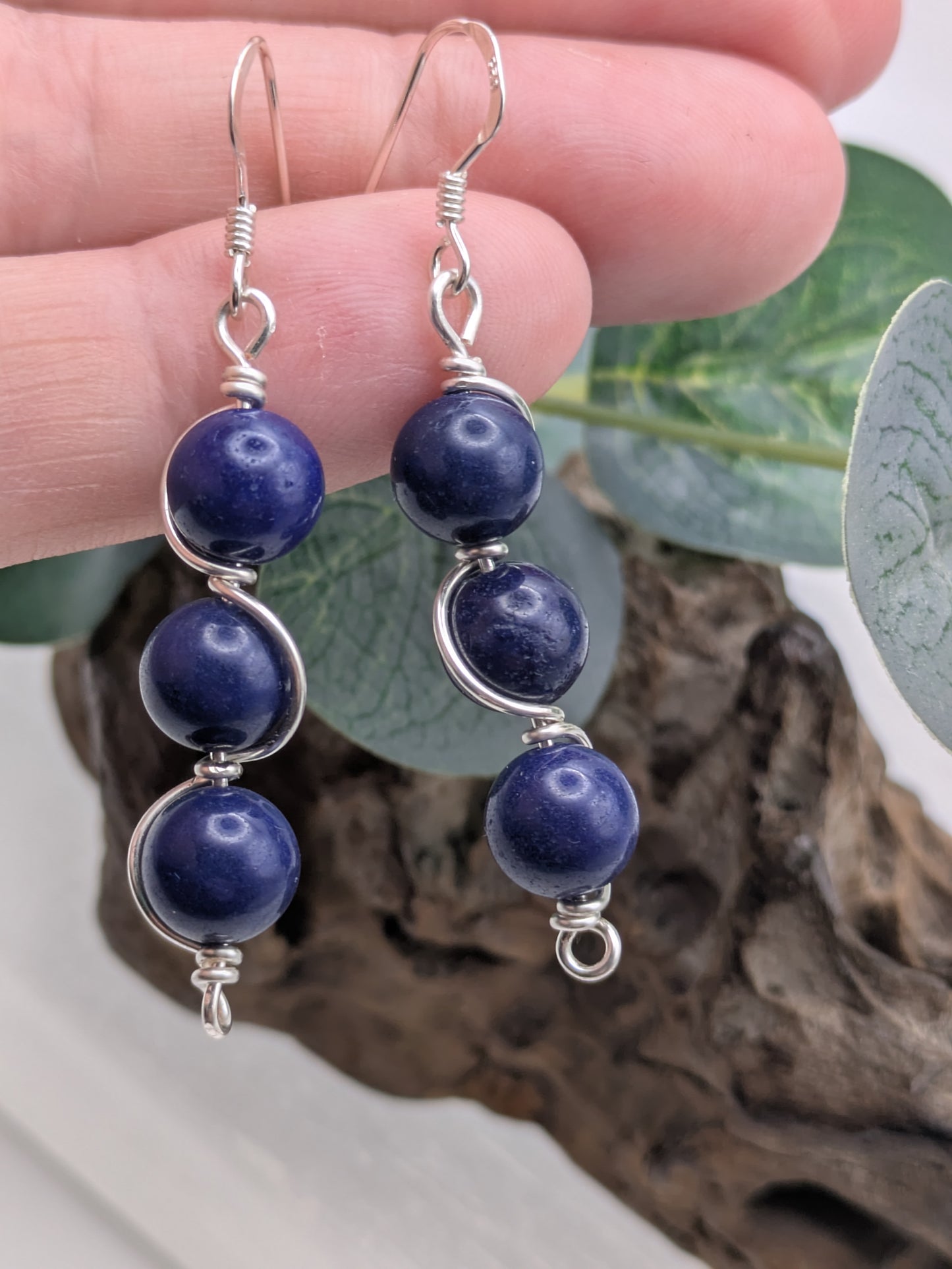 Close-up of silver wrapped Lapis Lazuli earrings with three deep blue gemstone beads in a vertical drop design, displayed on a neutral background.