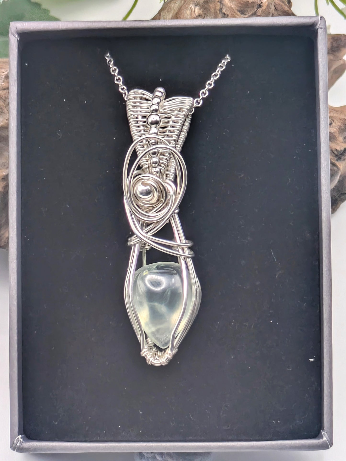 A silver wire wrapped pendant with a light green prehnite gemstone. The pendant is hanging from a silver chain.