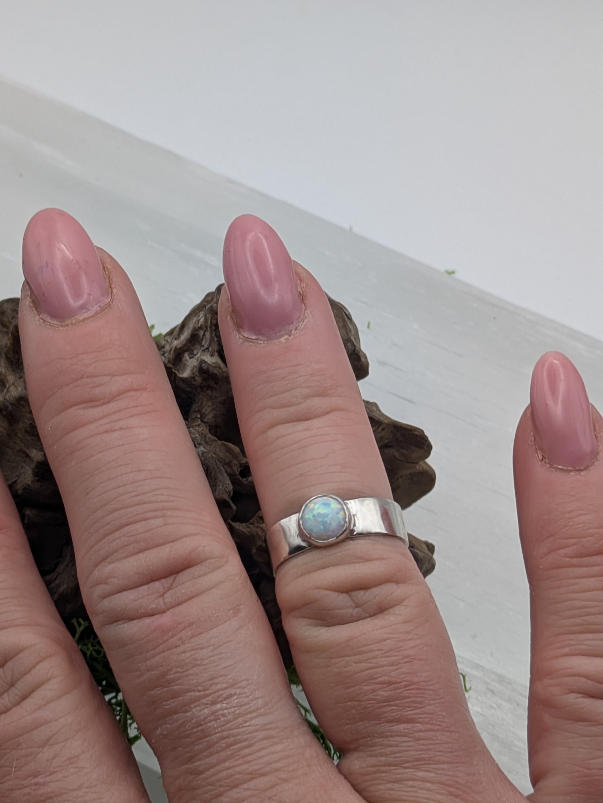 Hand wearing a silver ring with a mesmerising opal gemstone on a neutral background