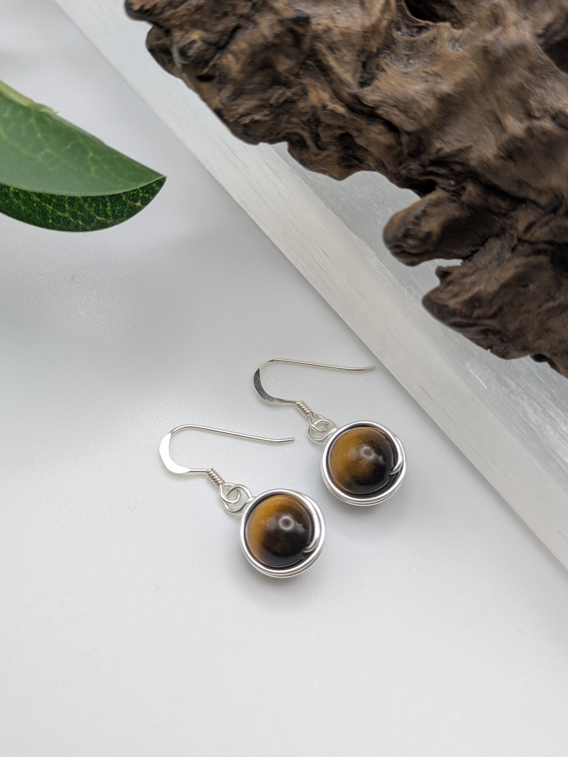 Silver earrings featuring round Tiger’s Eye gemstones with golden-brown chatoyancy, displayed on a crystal slab.