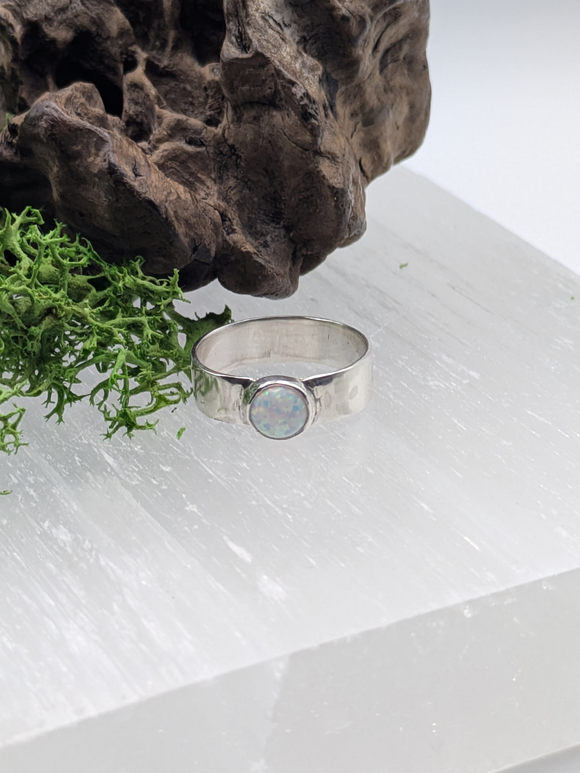 Silver ring with a mesmerising opal stone  on a white surface with greenery