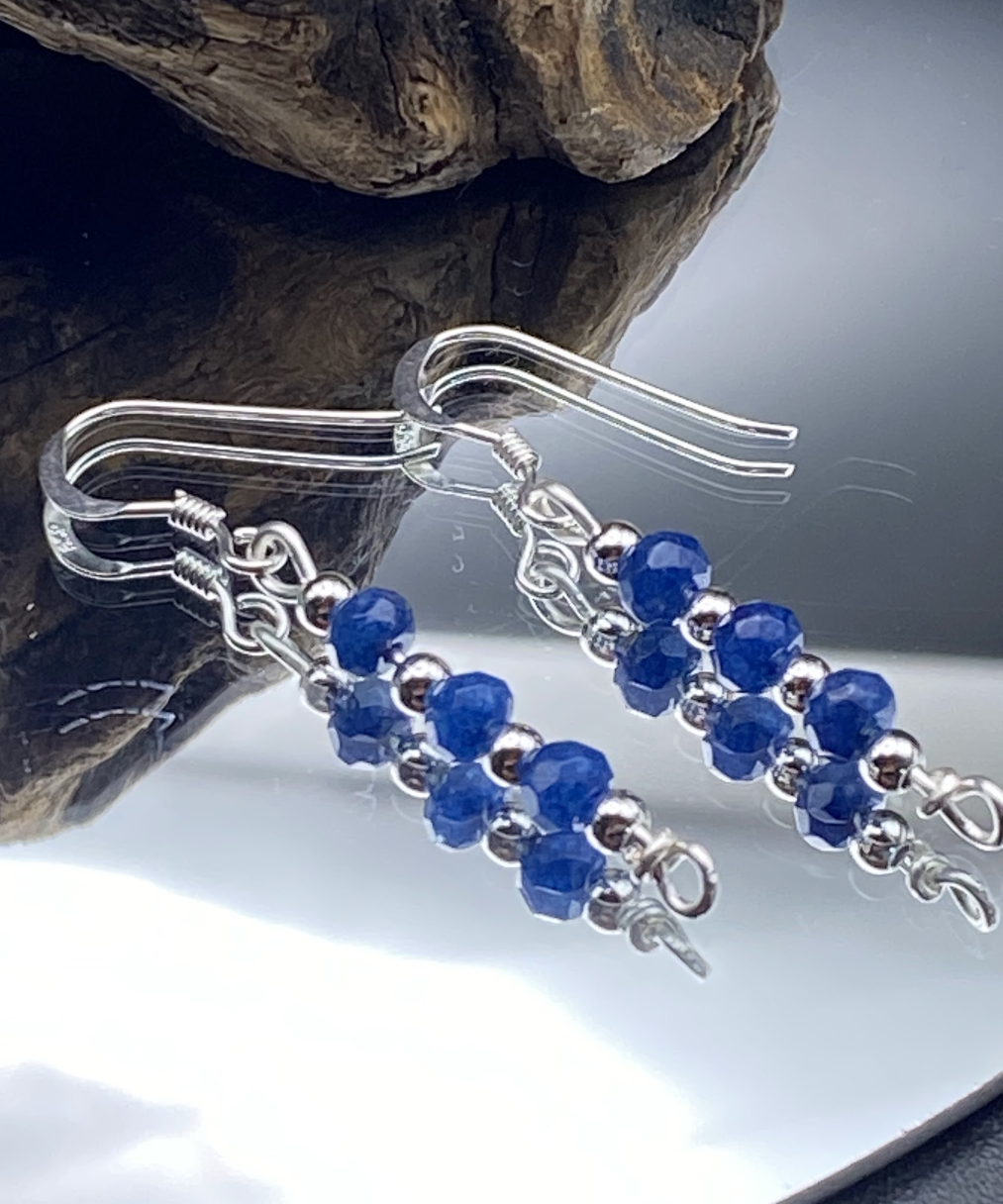 Close-up of dainty sapphire blue and silver bead drop earrings, displayed on a soft neutral background.