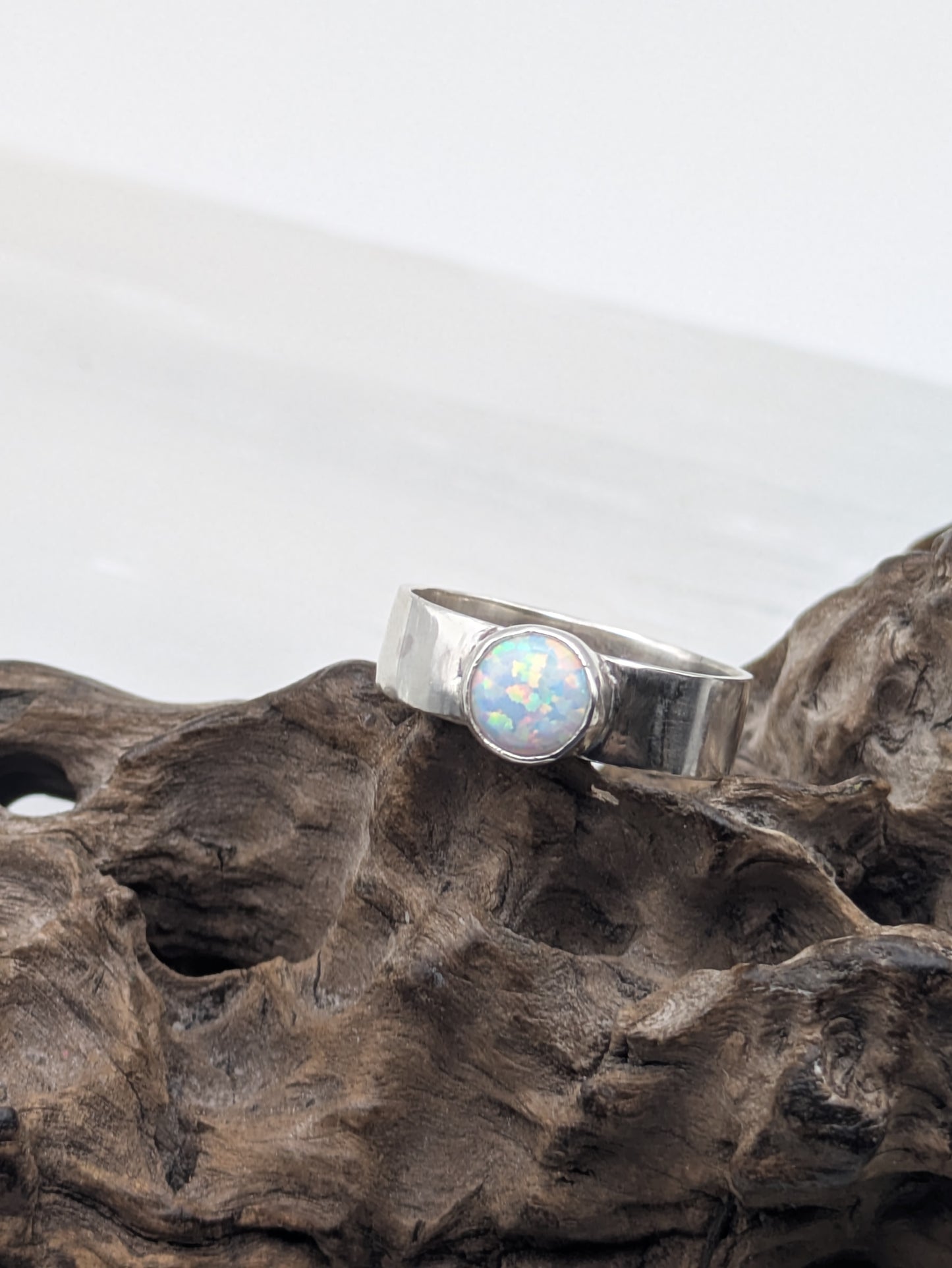 Silver ring with a opal stone on a textured wooden surface