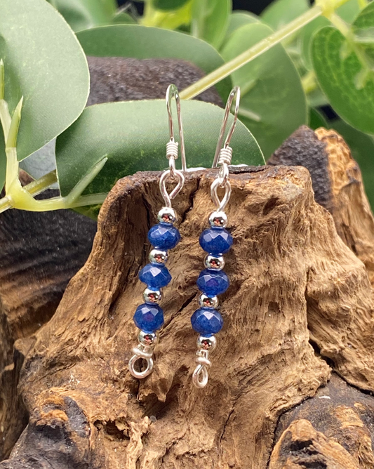 Close-up of dainty sapphire blue and silver bead drop earrings, displayed on a soft neutral background.