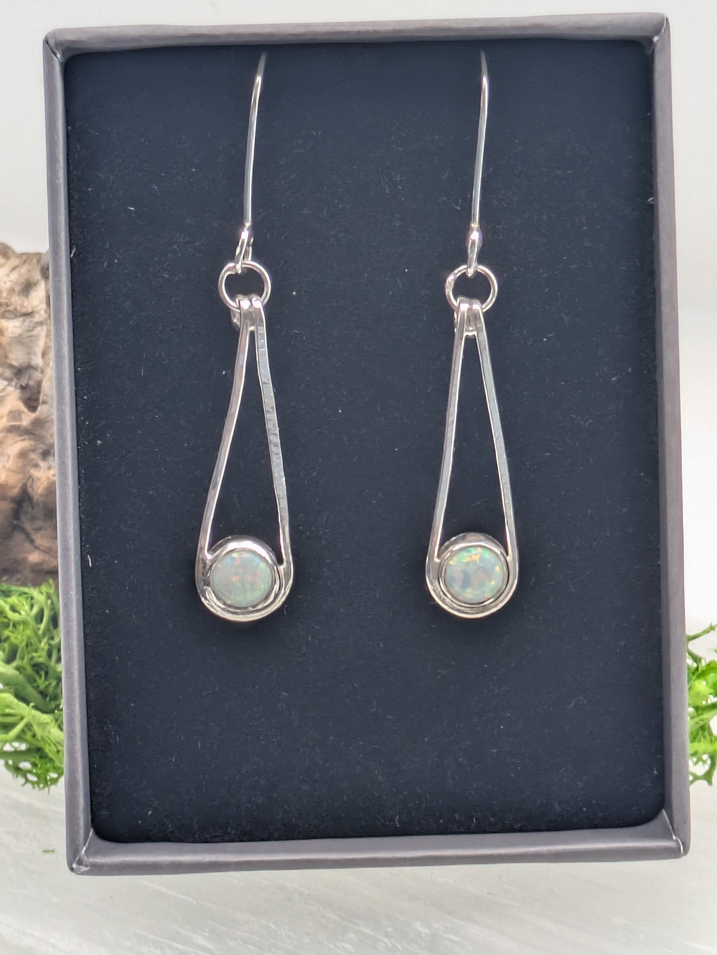 Close-up of fully hallmarked sterling silver earrings with iridescent Kyocera opals glowing in soft pink and blue tones, displayed on a neutral background.