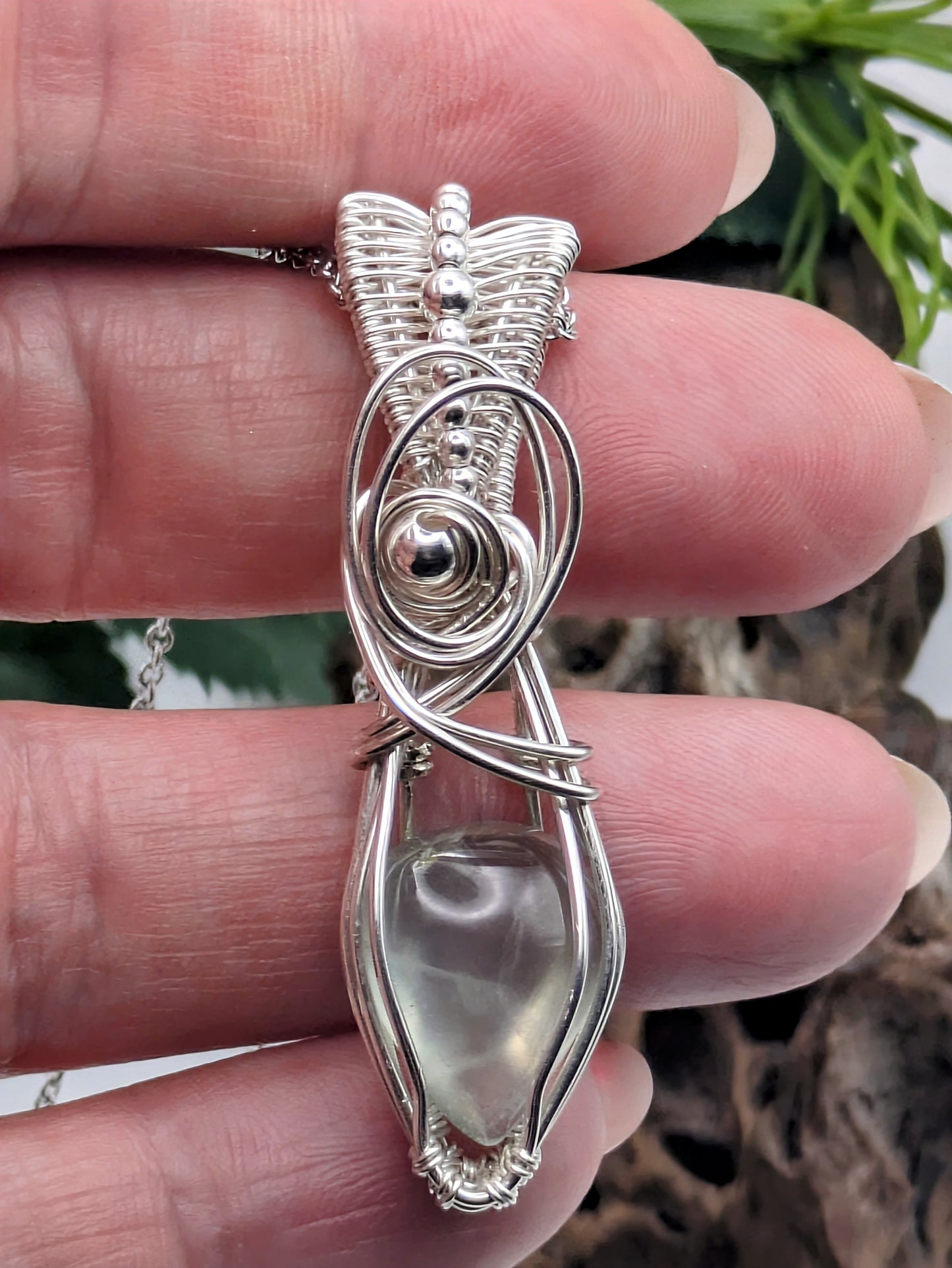 A silver wire wrapped pendant with a light green prehnite gemstone. The pendant is hanging from a silver chain.