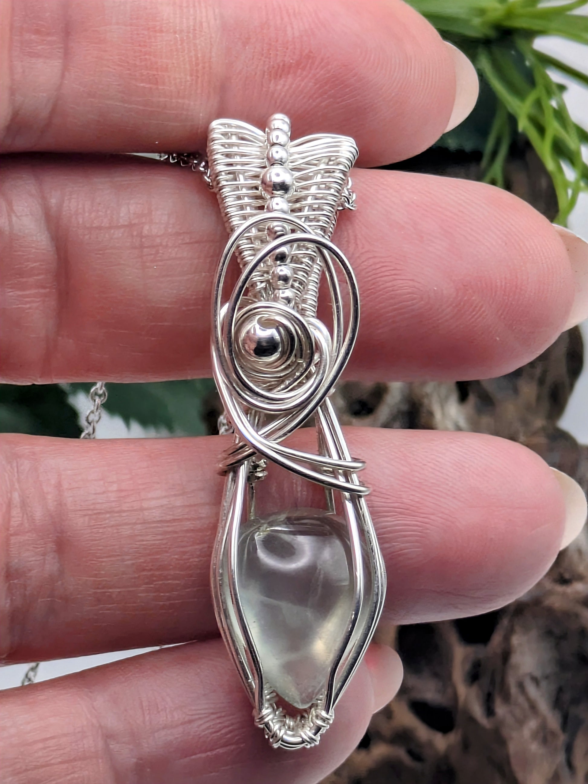 A silver wire wrapped pendant with a light green prehnite gemstone. The pendant is hanging from a silver chain.