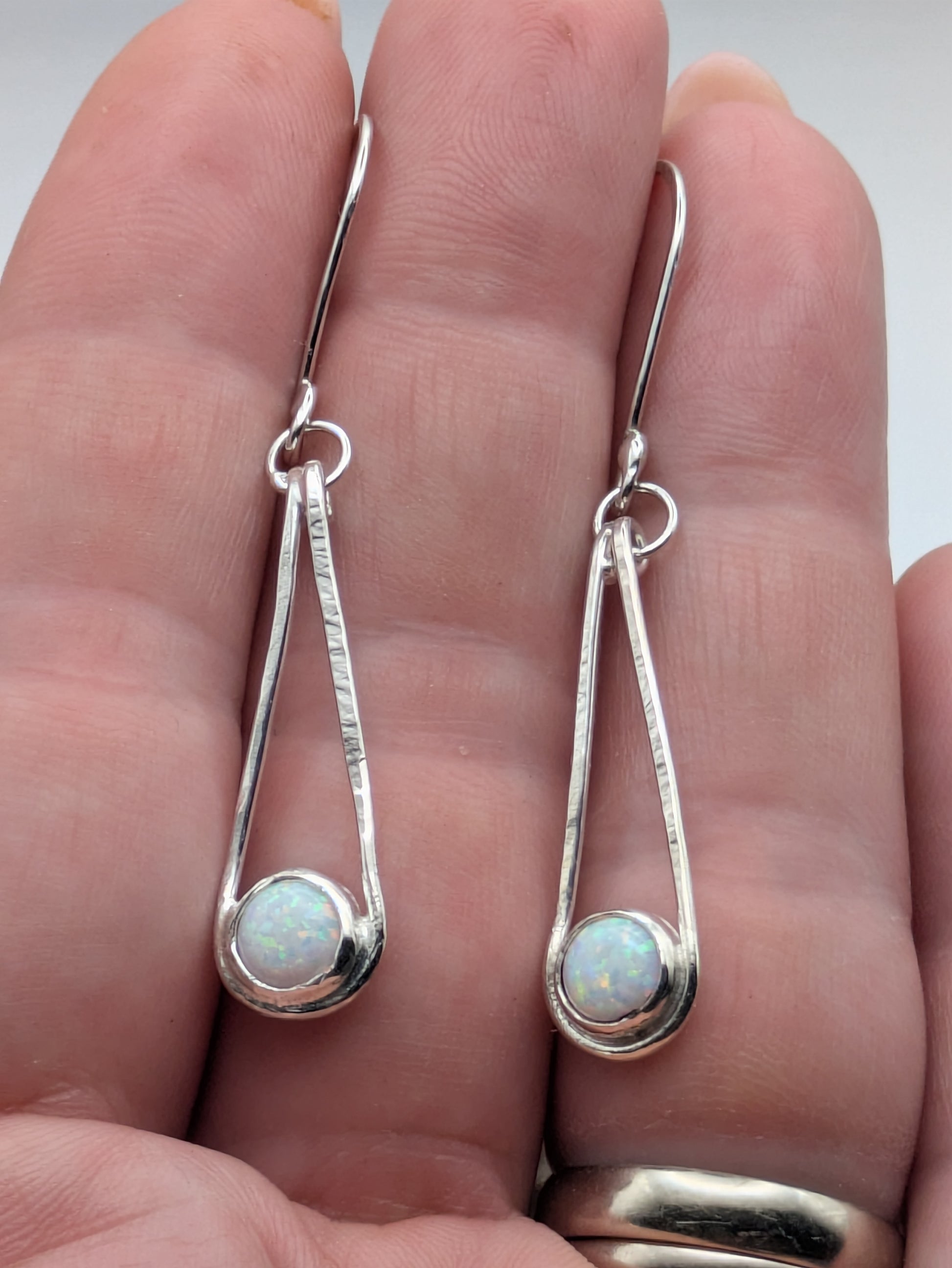 Close-up of fully hallmarked sterling silver earrings with iridescent Kyocera opals glowing in soft pink and blue tones, displayed on a neutral background.