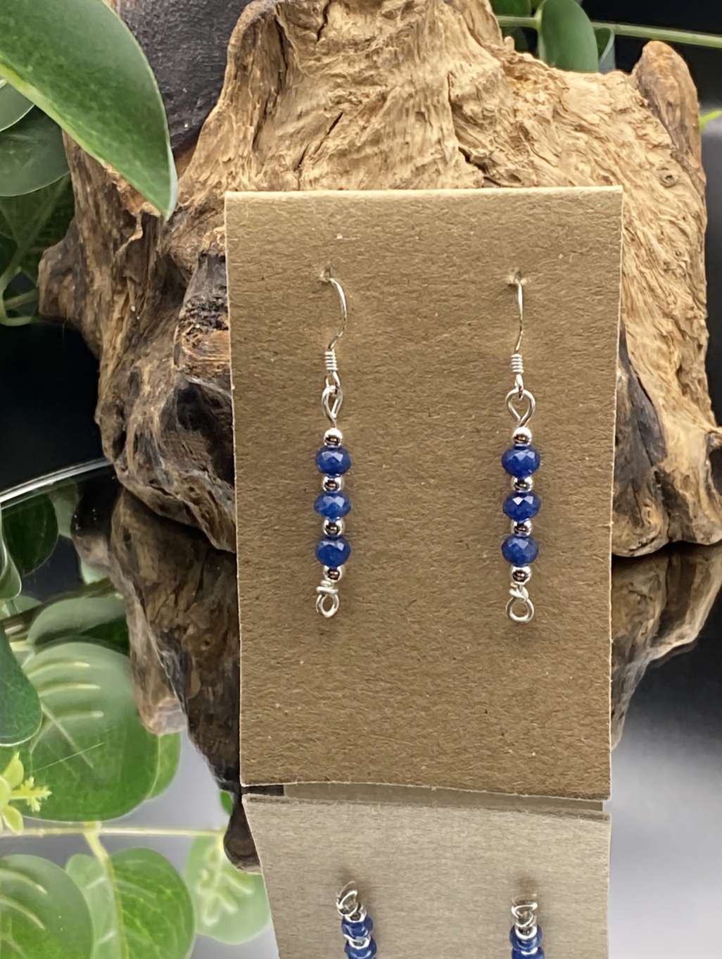 Close-up of dainty sapphire blue and silver bead drop earrings, displayed on a soft neutral background.