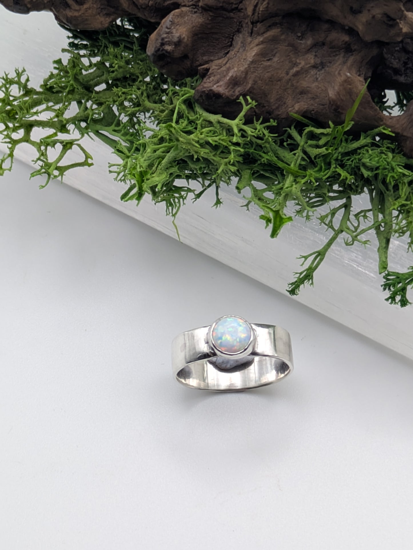 Silver ring with a central gemstone on a white surface with greenery in the background