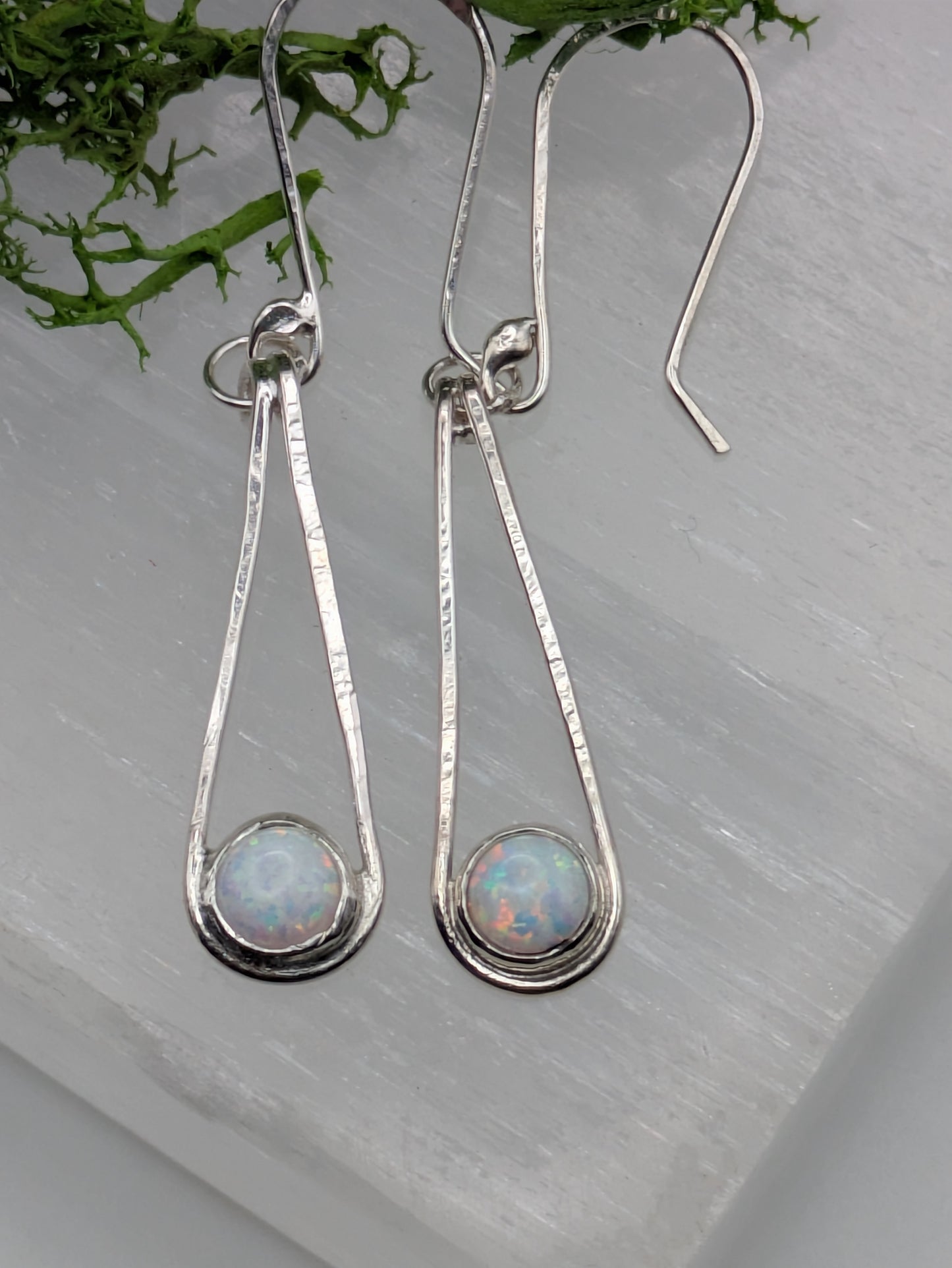 Close-up of fully hallmarked sterling silver earrings with iridescent Kyocera opals glowing in soft pink and blue tones, displayed on a neutral background.