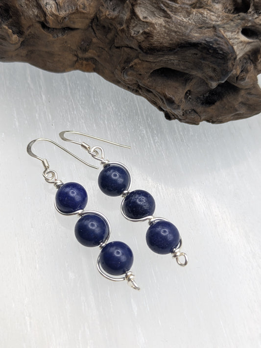 Close-up of silver wrapped Lapis Lazuli earrings with three deep blue gemstone beads in a vertical drop design, displayed on a neutral background.