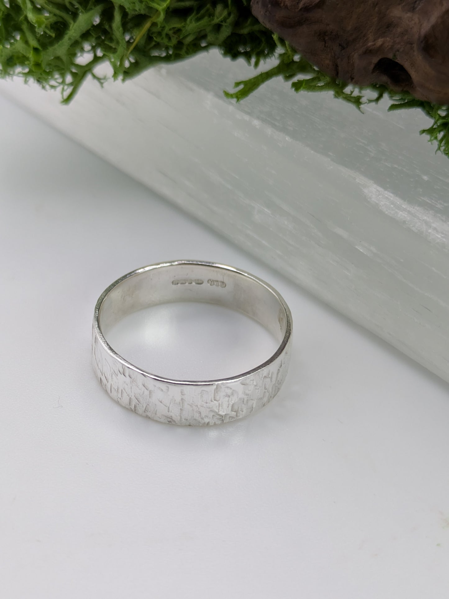 Hallmarked Sterling Silver ring with a textured design on a white surface with greenery in the background