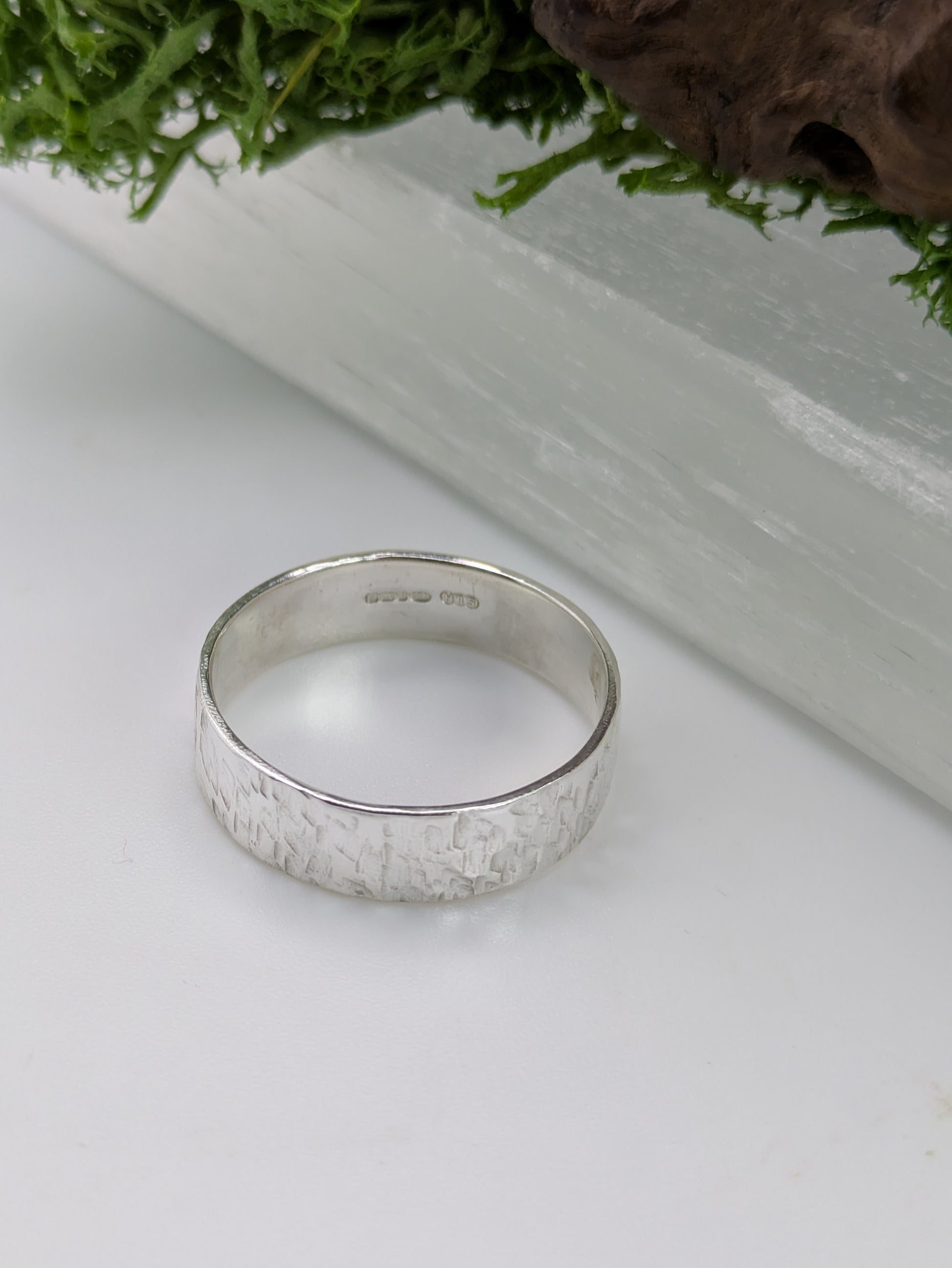 Hallmarked Sterling Silver ring with a textured design on a white surface with greenery in the background
