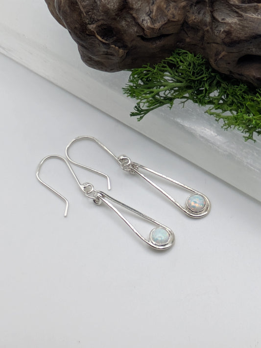 Close-up of fully hallmarked sterling silver earrings with iridescent Kyocera opals glowing in soft pink and blue tones, displayed on a neutral background.