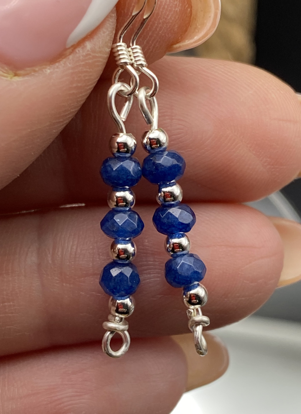 Close-up of dainty sapphire blue and silver bead drop earrings, displayed on a soft neutral background.