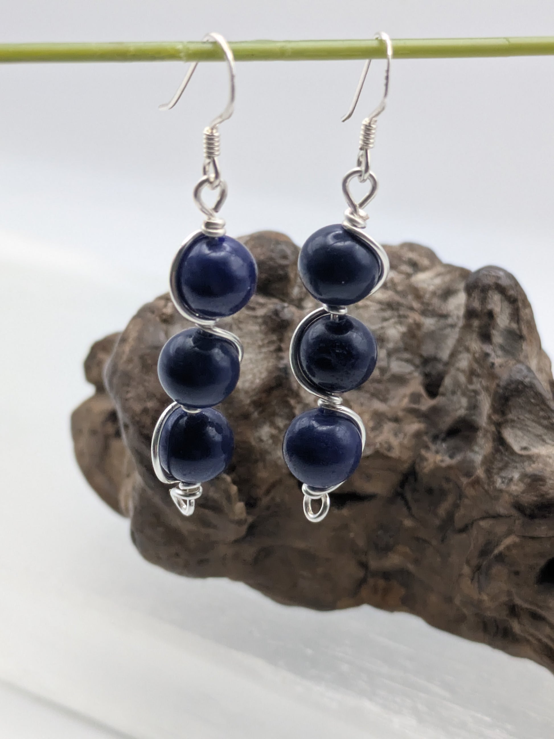 Close-up of silver wrapped Lapis Lazuli earrings with three deep blue gemstone beads in a vertical drop design, displayed on a neutral background.