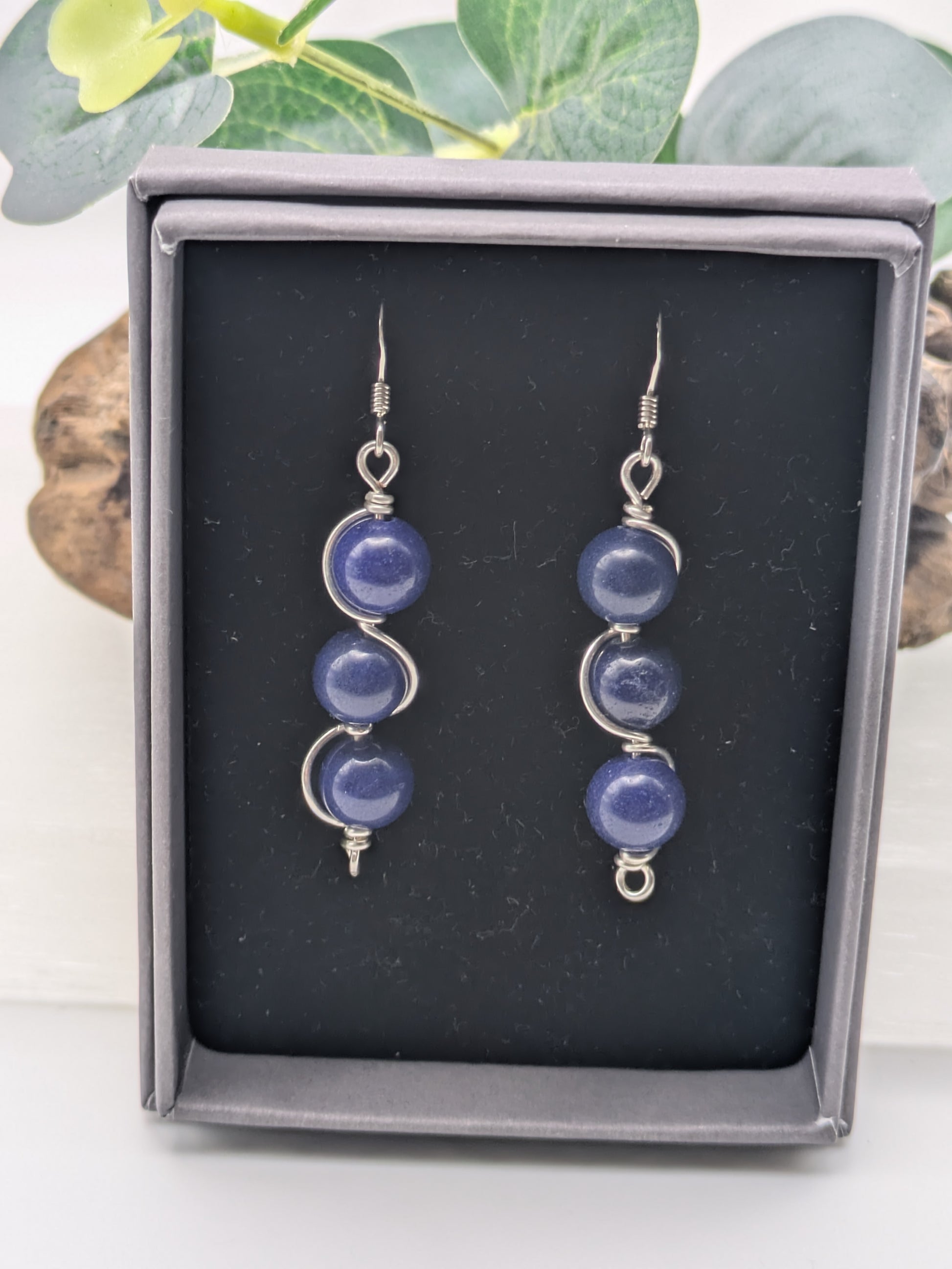 Close-up of silver wrapped Lapis Lazuli earrings with three deep blue gemstone beads in a vertical drop design, displayed on a neutral background.