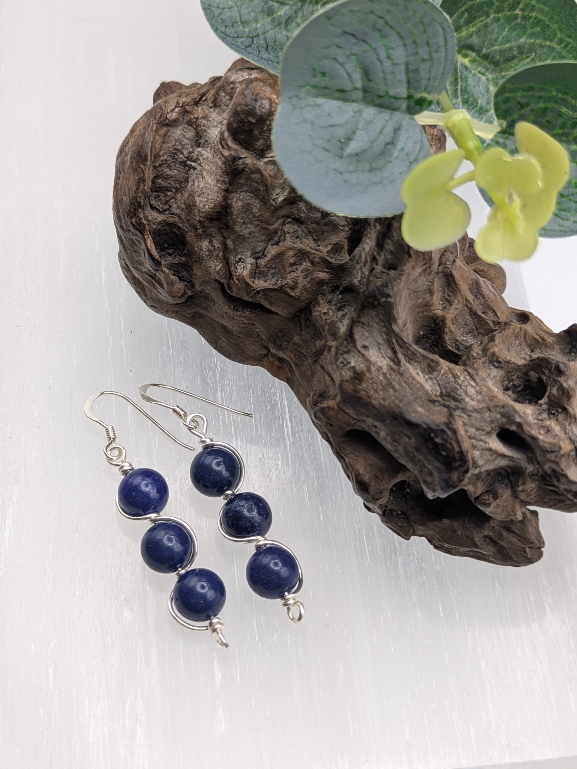 Close-up of silver wrapped Lapis Lazuli earrings with three deep blue gemstone beads in a vertical drop design, displayed on a neutral background.