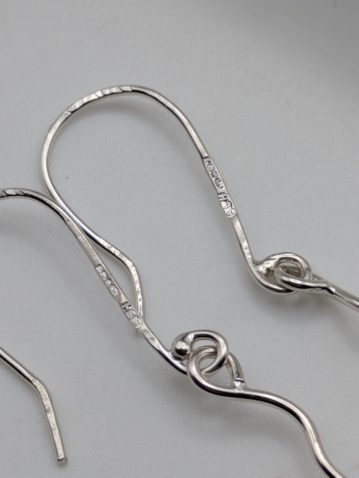 Close-up of fully hallmarked sterling silver earrings with iridescent Kyocera opals glowing in soft pink and blue tones, displayed on a neutral background.