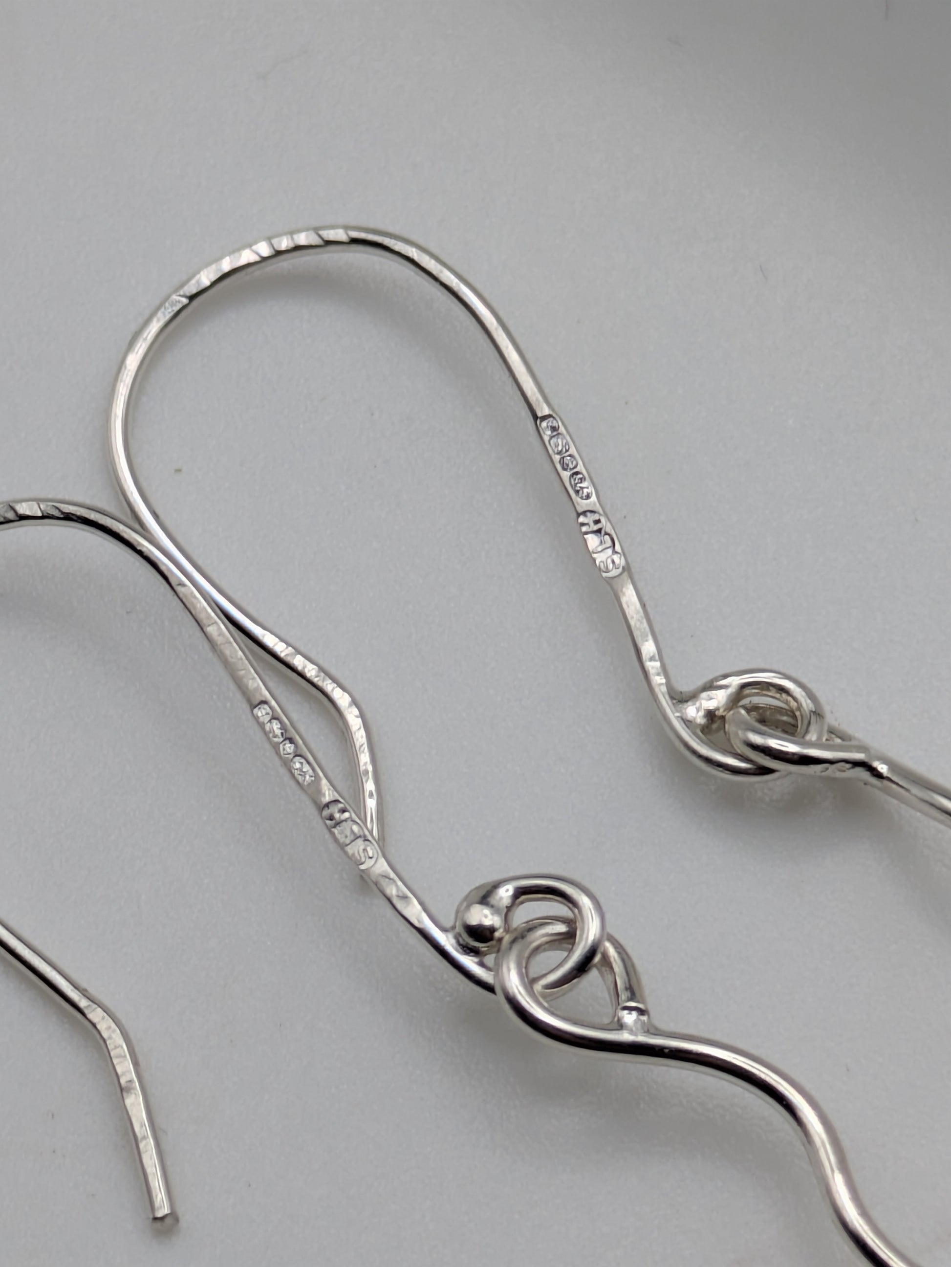 Close-up of fully hallmarked sterling silver earrings with iridescent Kyocera opals glowing in soft pink and blue tones, displayed on a neutral background.