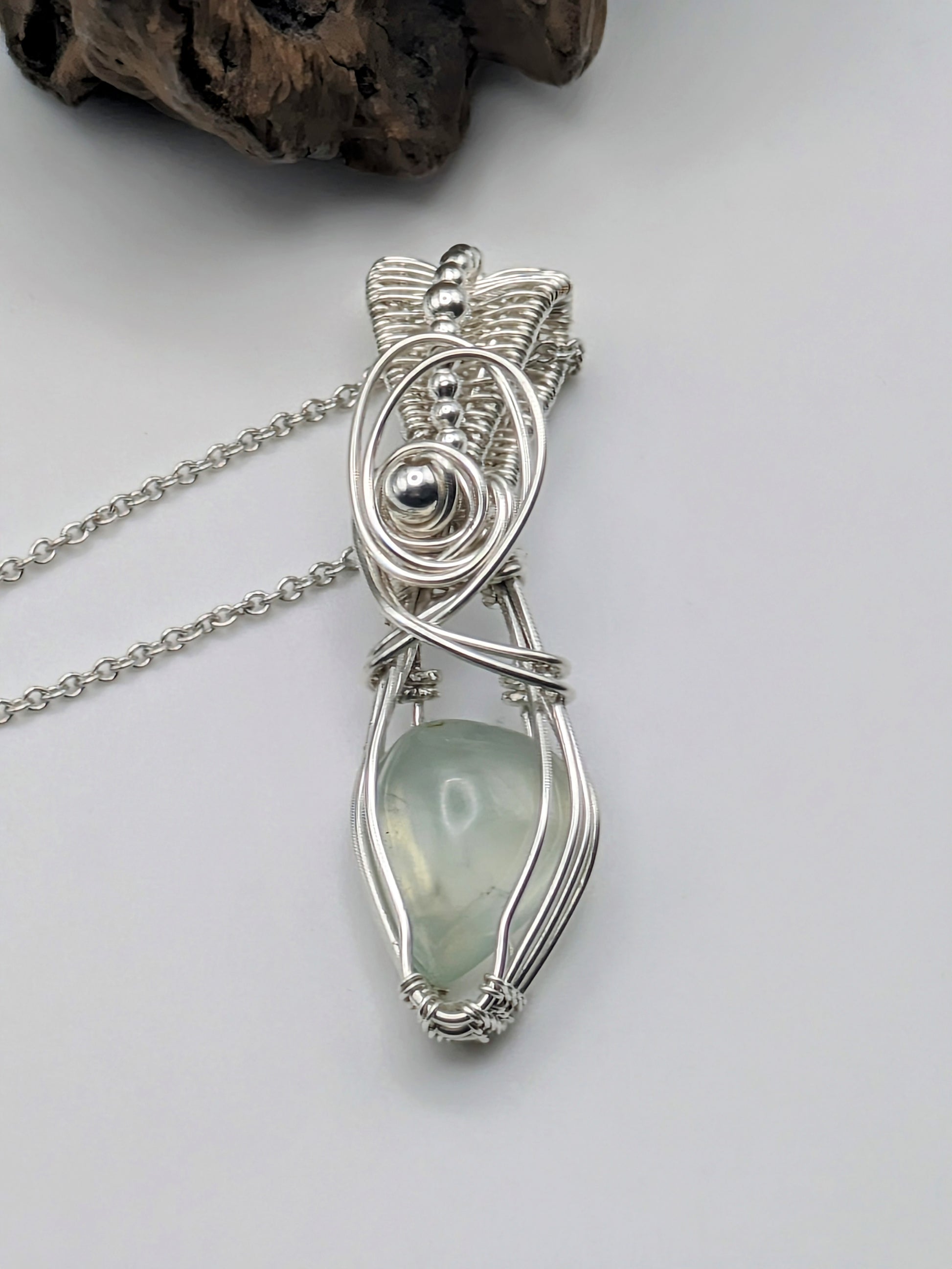 A silver wire wrapped pendant with a light green prehnite gemstone. The pendant is hanging from a silver chain.