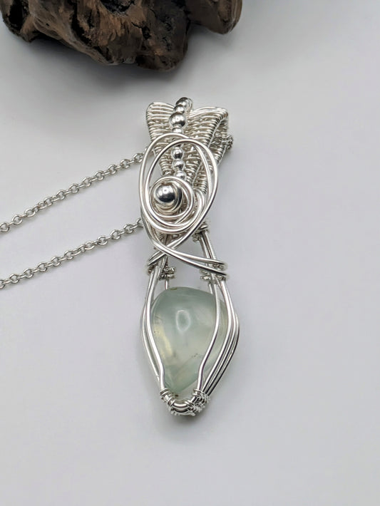A silver wire wrapped pendant with a light green prehnite gemstone. The pendant is hanging from a silver chain.
