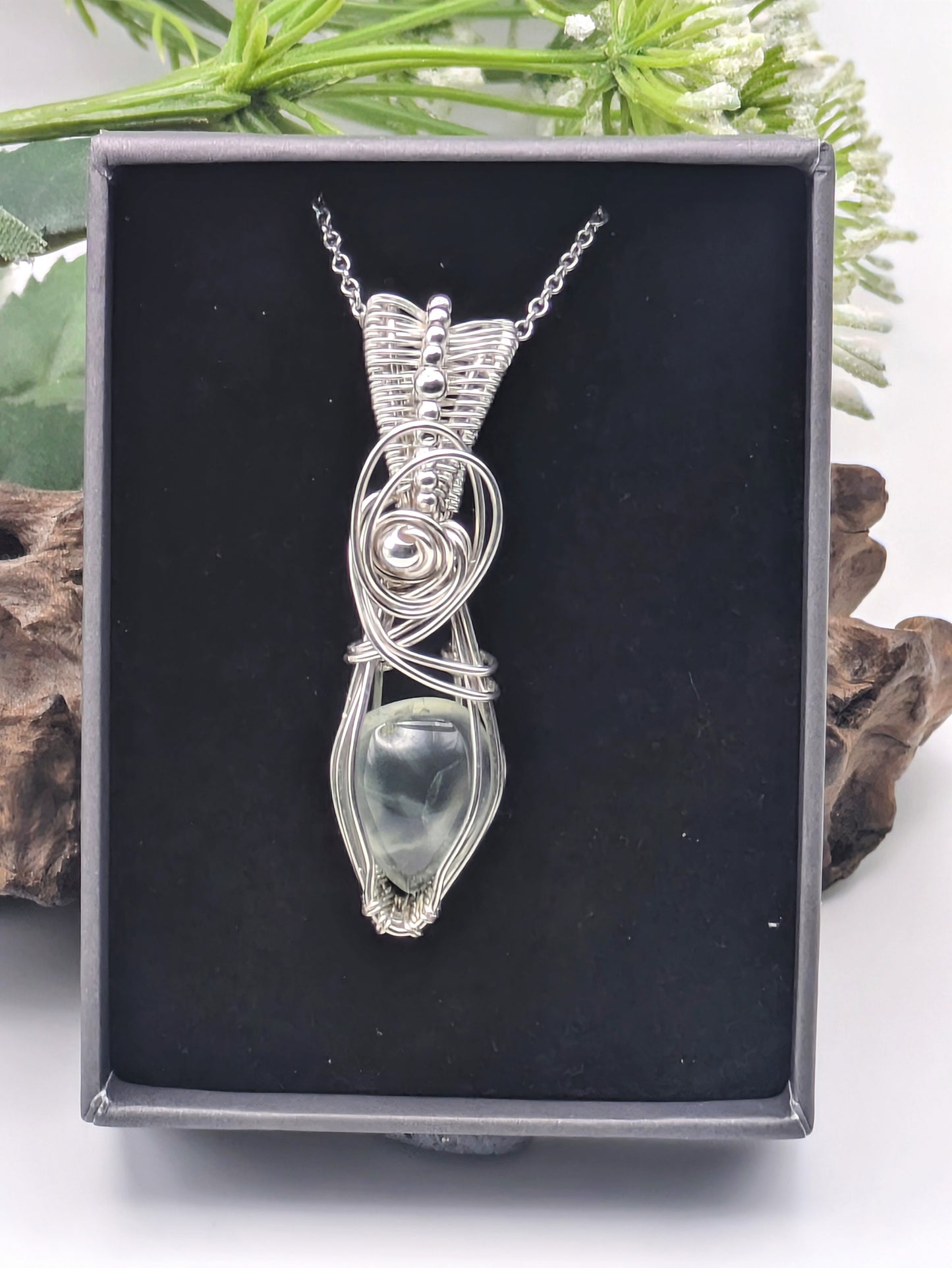 A silver wire wrapped pendant with a light green prehnite gemstone. The pendant is hanging from a silver chain.