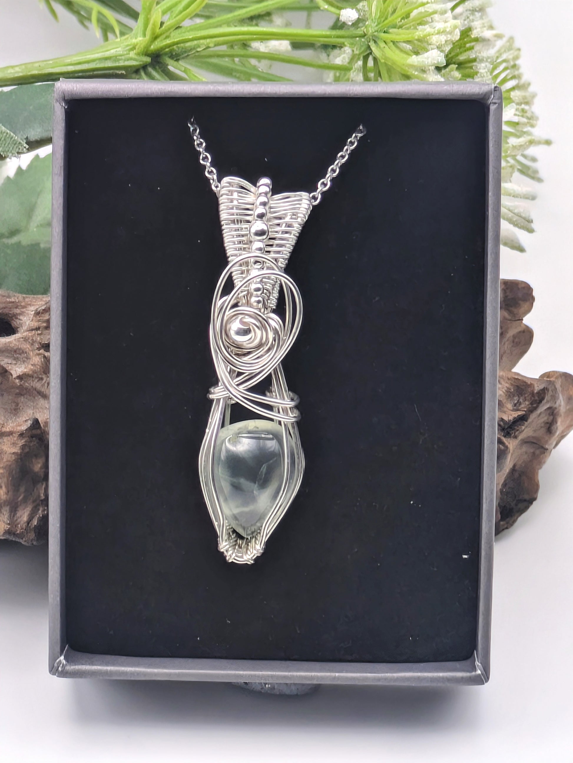 A silver wire wrapped pendant with a light green prehnite gemstone. The pendant is hanging from a silver chain.