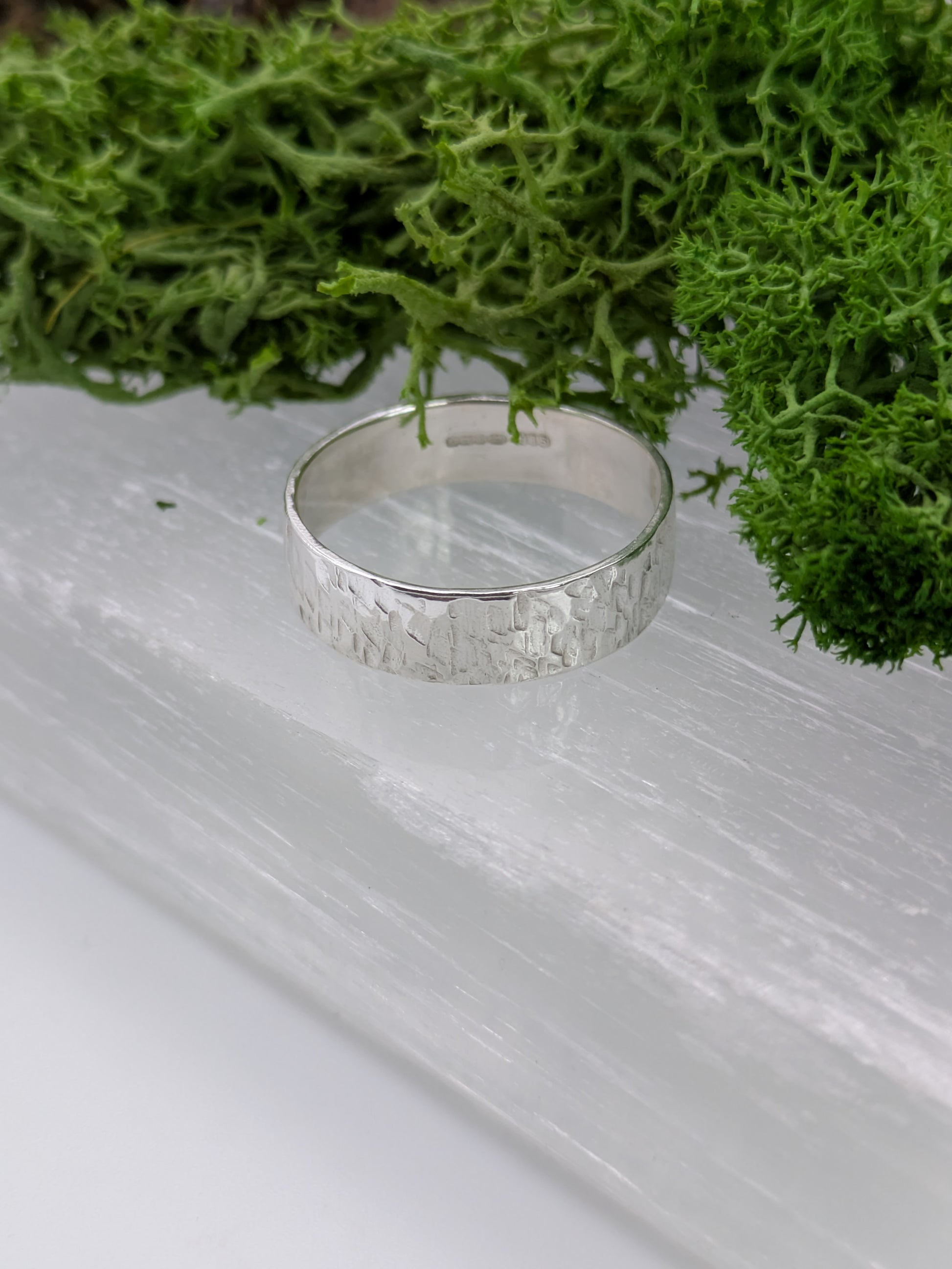 Textured Silver ring on a clear crystal surface with green moss in the background