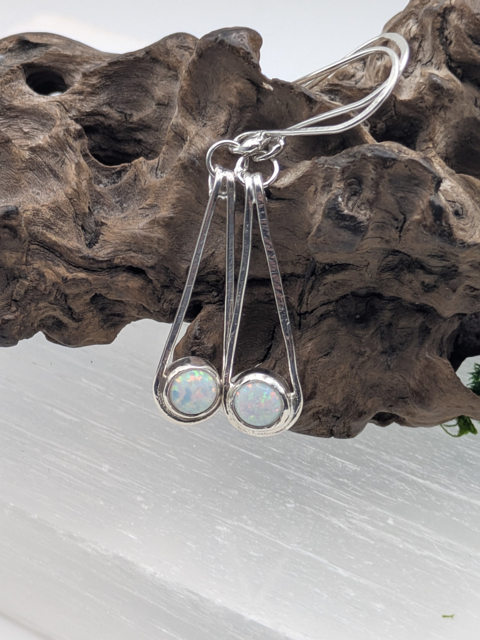 Close-up of fully hallmarked sterling silver earrings with iridescent Kyocera opals glowing in soft pink and blue tones, displayed on a neutral background.