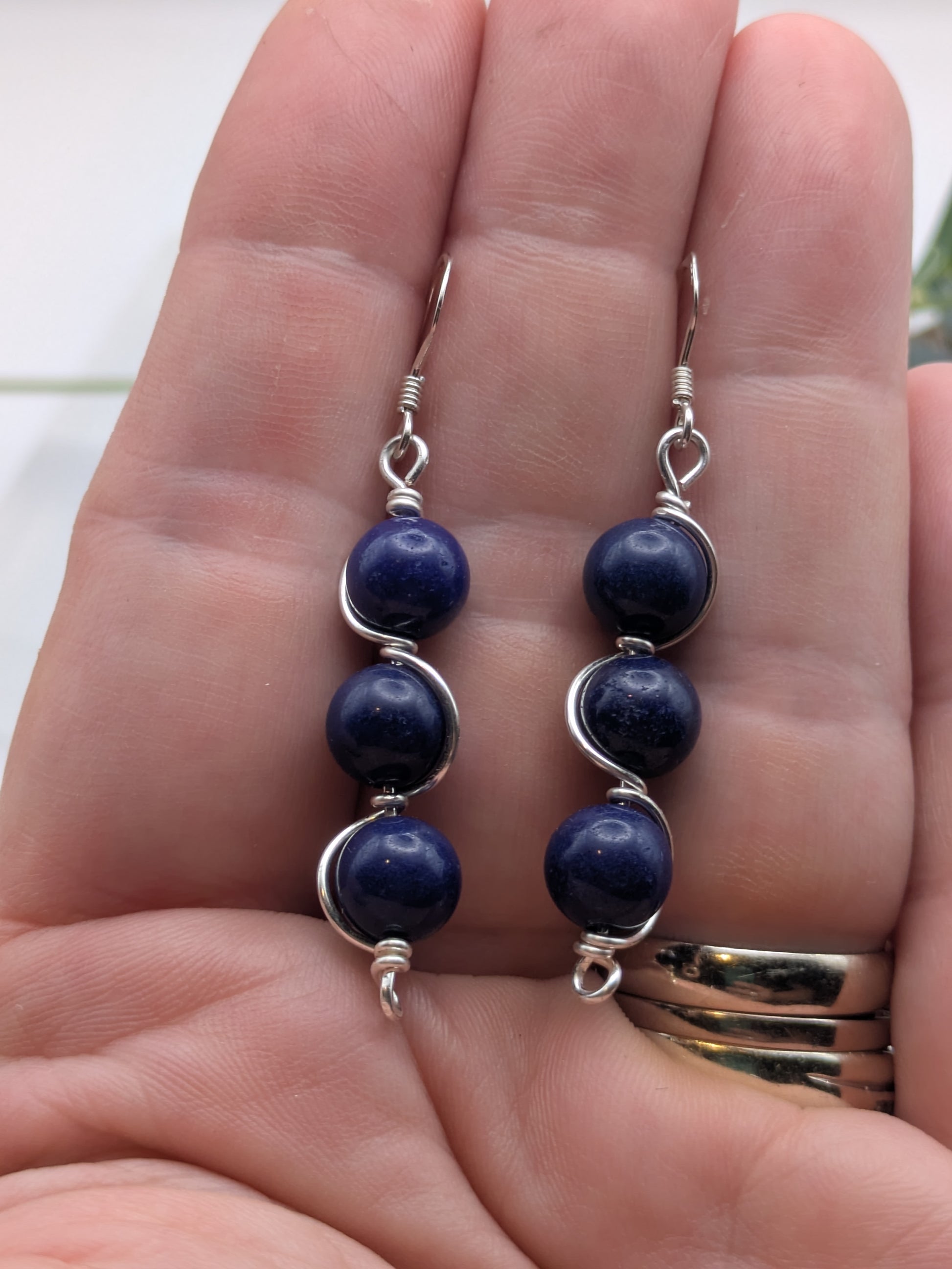 Close-up of silver wrapped Lapis Lazuli earrings with three deep blue gemstone beads in a vertical drop design, displayed on a neutral background.
