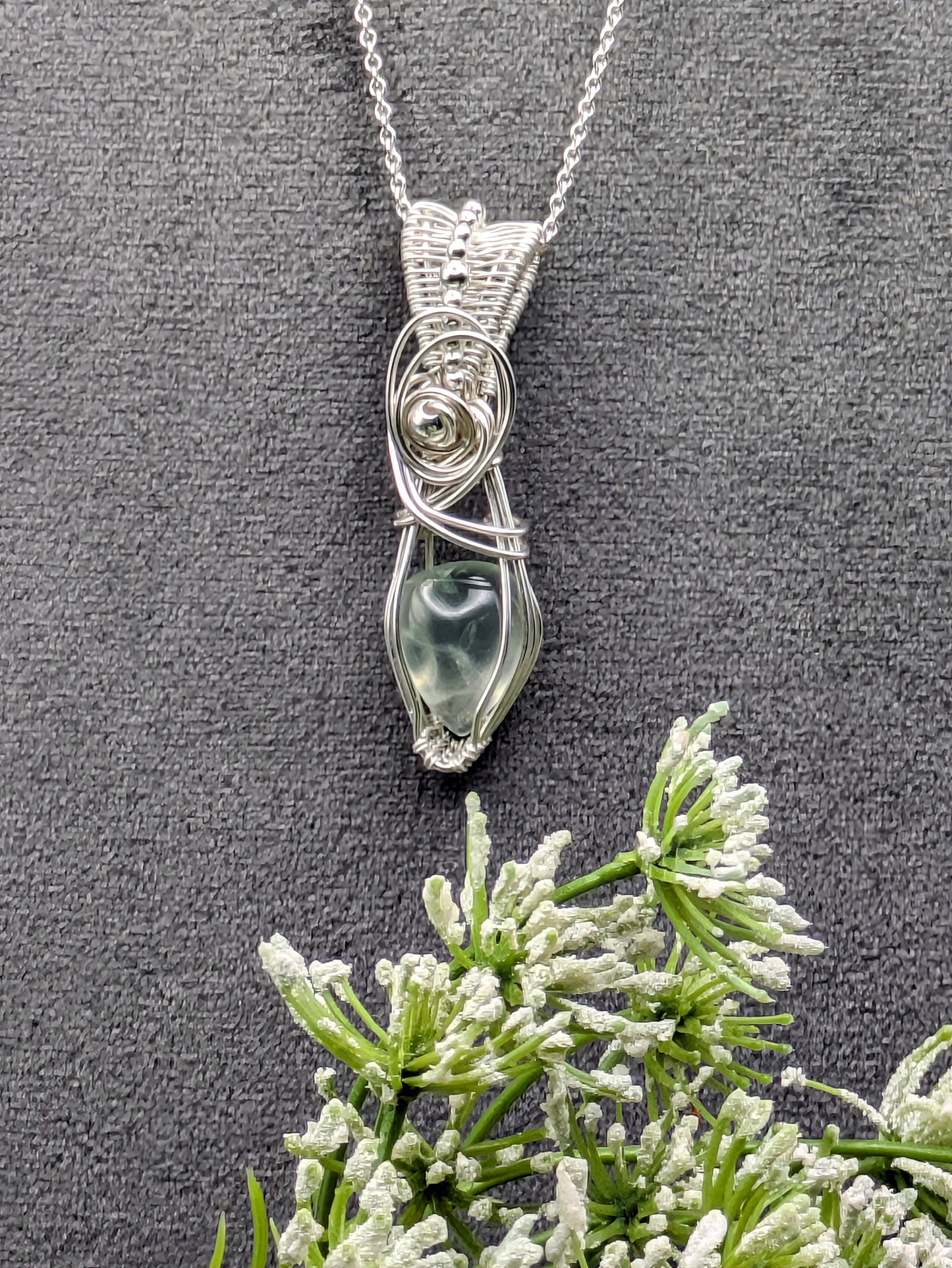 A silver wire wrapped pendant with a light green prehnite gemstone. The pendant is hanging from a silver chain.