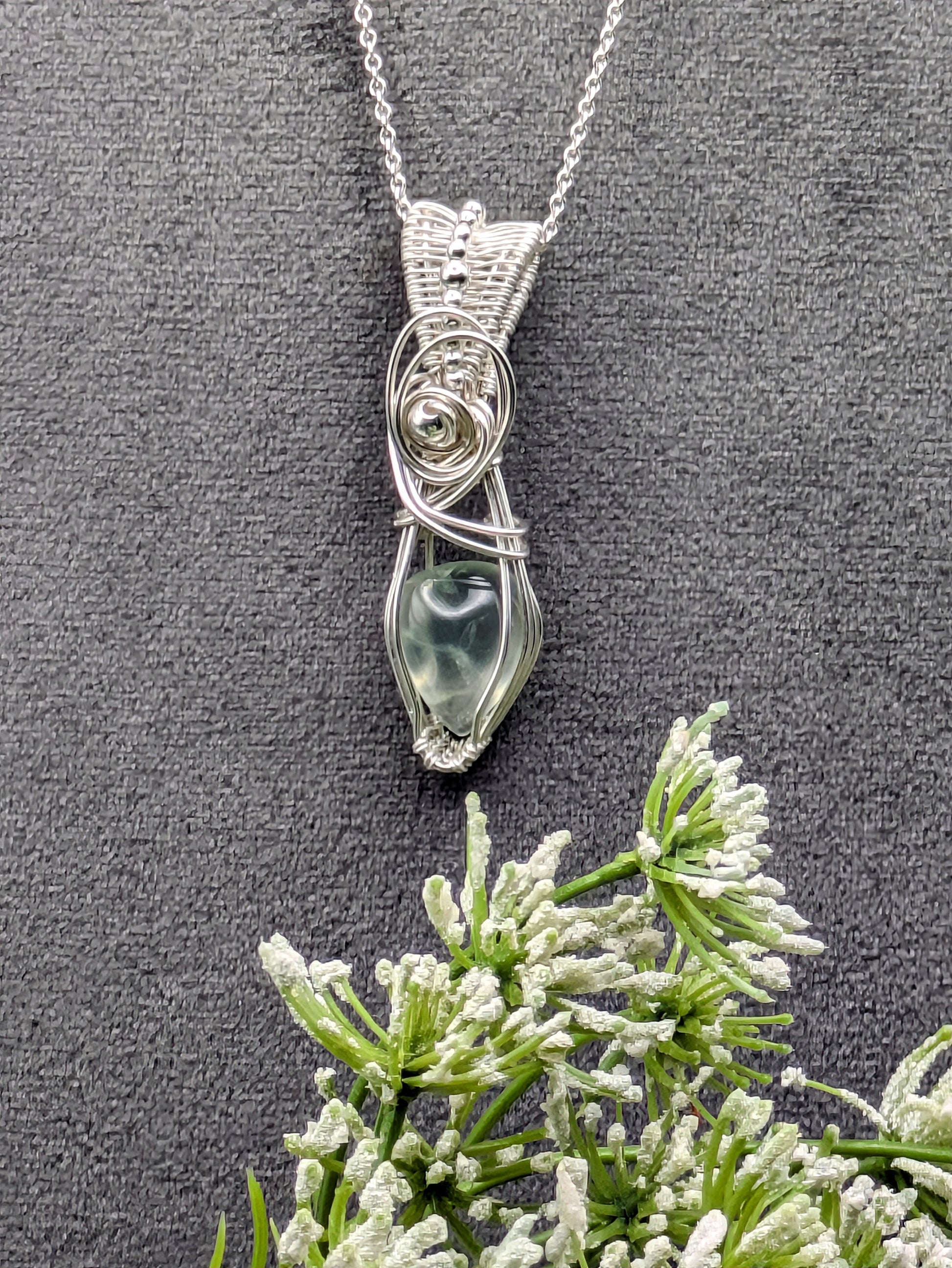 A silver wire wrapped pendant with a light green prehnite gemstone. The pendant is hanging from a silver chain.