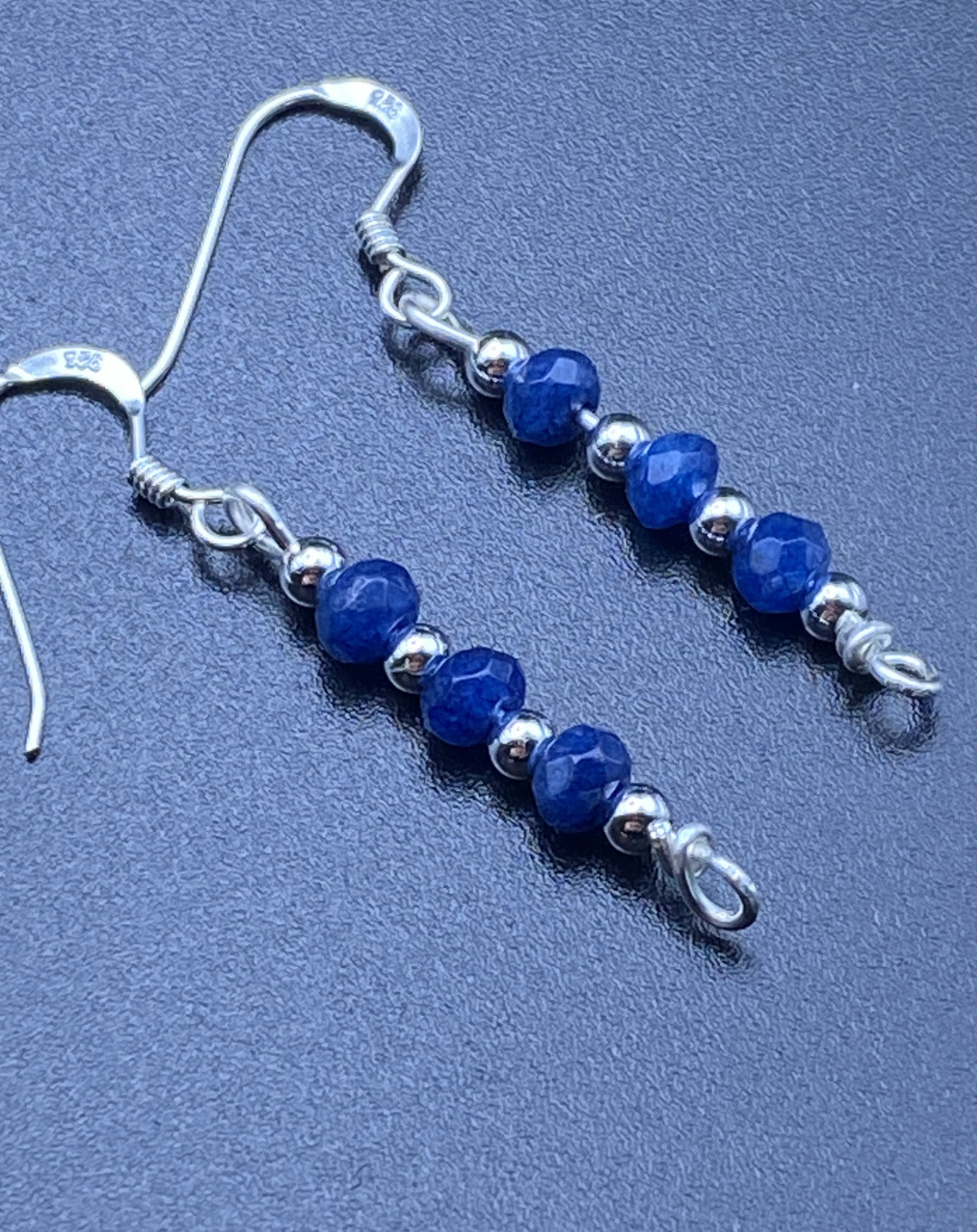 Close-up of dainty sapphire blue and silver bead drop earrings, displayed on a soft neutral background.