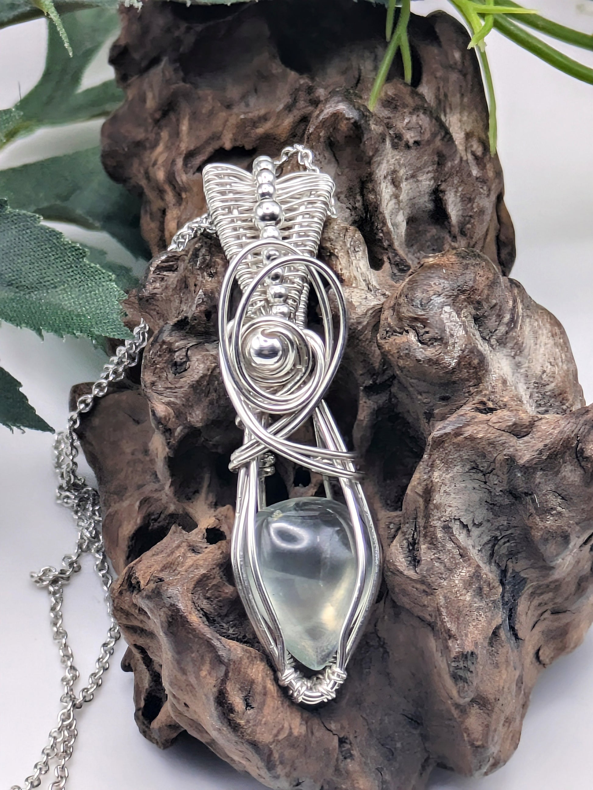 A silver wire wrapped pendant with a light green prehnite gemstone. The pendant is hanging from a silver chain.